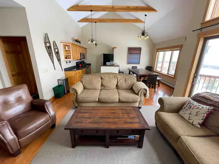 A living room with wooden floors, beige couches, a wooden coffee table, and a kitchen.